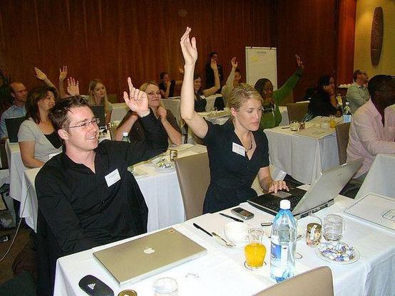 right way to vote: photograph of conference attendees sitting in front of tables, raising their hands to vote