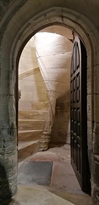 Eine offene Kasettenholztür lässt die ersten Stufen einer Sandstein Wendeltreppe erkennen.