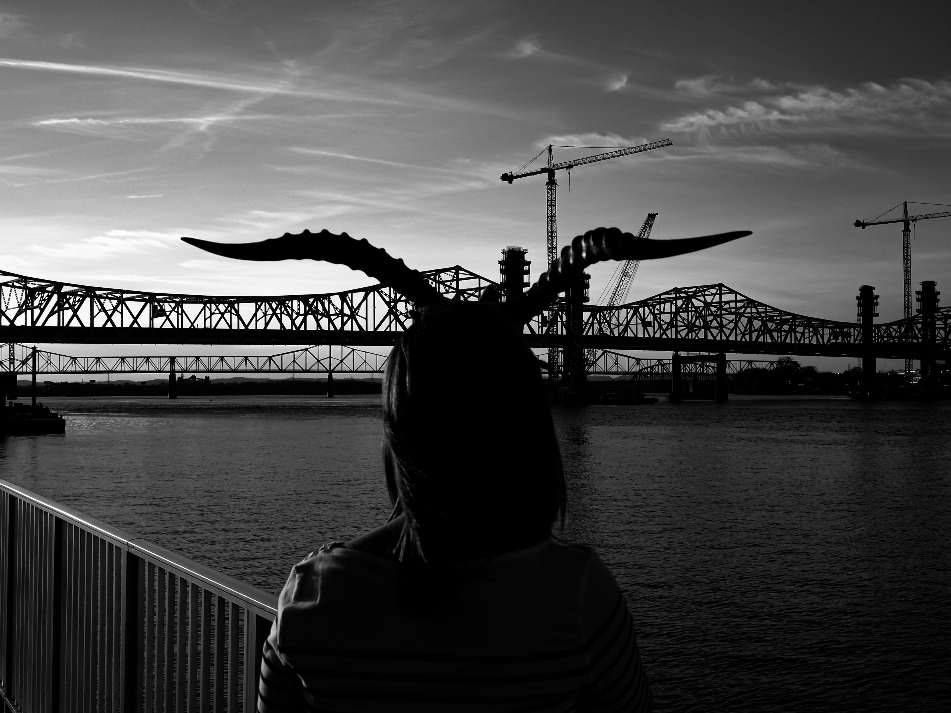 black and white photo of someone wearing horns while staring at a bridge