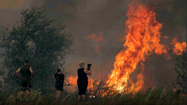 toeristen staan met de handen in de zij naar een felle bosbrand te kijken en er foto's van te maken