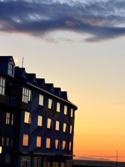 A sunset under some dark clouds is reflected off the rows of big windows on a building to the left