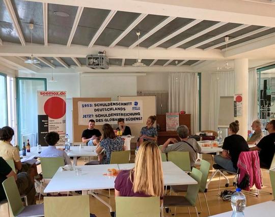 Three people reading in front of an audience in room. 