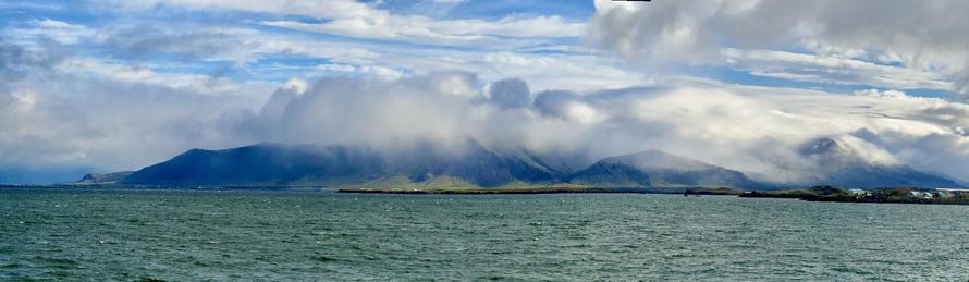 A panorama of Mt. Esja. Slightly choppy water in the foreground and clouds obscuring the top of the mountain. 