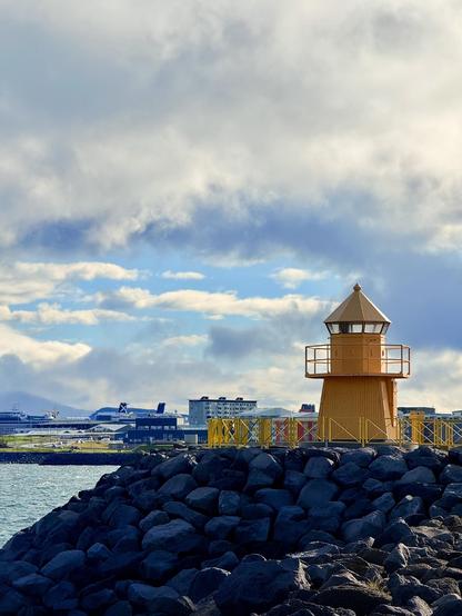 A small yellow lighthouse with dramatic clouds behind it and the eastern part of the city