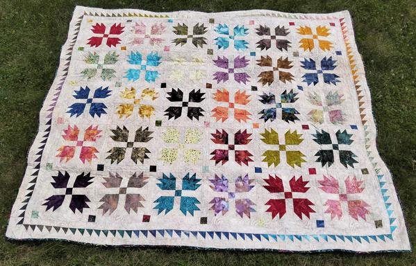 a quilt, it is multi-colored angular bearpaw designs on a light background, rows of thin triangles for the borders of it 