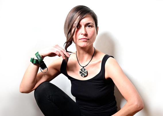 Ein Pressebild der Singer-Songwriterin Pauli. Sie trägt ein schwarzes Top und sitzt vor einem weißen Hintergrund. Am rechten Arm trägt sie grüne Bänder!