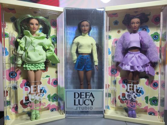 Left: Green variant Defa Lucy Love
Center: Defa Lucy Studio in yellow sweater and metallic blue shorts
Right: Purple variant Defa Lucy Love