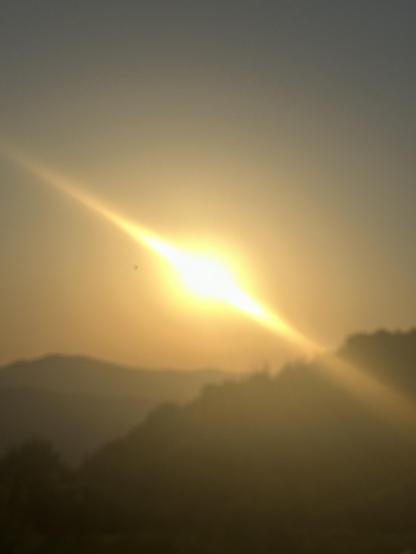 Puesta de sol, montañas, bruma fotográfica 
por estar desenfocado. 
Mucho calor, el sol parece arder en un cielo despejado, con dos resplandores diagonales que cruzan la foto. Sin piedad.