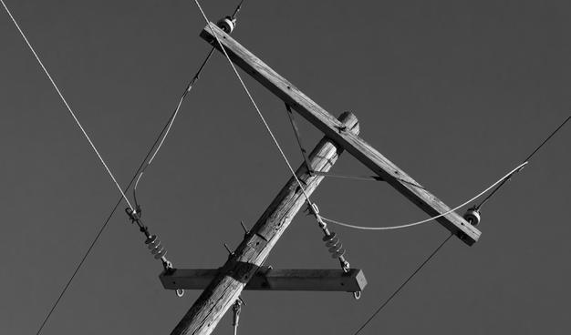 A wooden power pole enters a bit left of center and rises at a 45 degree angle to the upper right,  the main crossbar branched at the end at a (on paper) 90 degree andle and a bit lower down a smaller crossbar branches;   each crossbar has a pair of wires on it and wires bridge the two lines to split power from the main line to a subsidiary