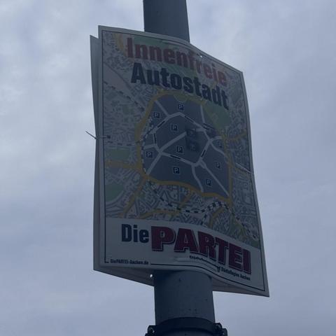 Wahlplakat der Partei "Die Partei". Zu sehen ist eine Karte von Aachen. Innerhalb des Alleenrings ist bis auf die Hauptverkehrswege alles grau und als Parkplatz deklariert. Die Überschrift des Plakats ist "Innenfreie Autostadt".