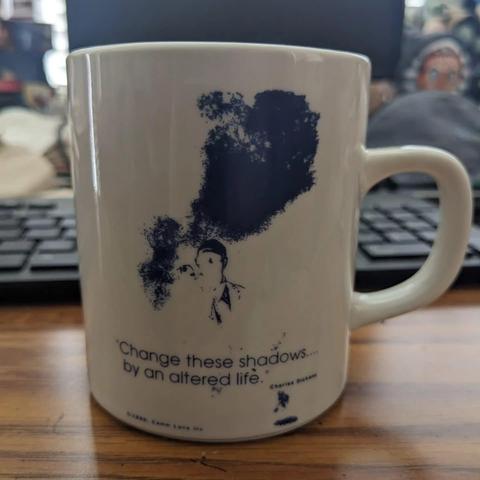 Mug with fuzzy blue cloudy image with the vague outline of a man pointing a finger forward. Text says "Change these shadows... by an altered life." Charles Dickens 