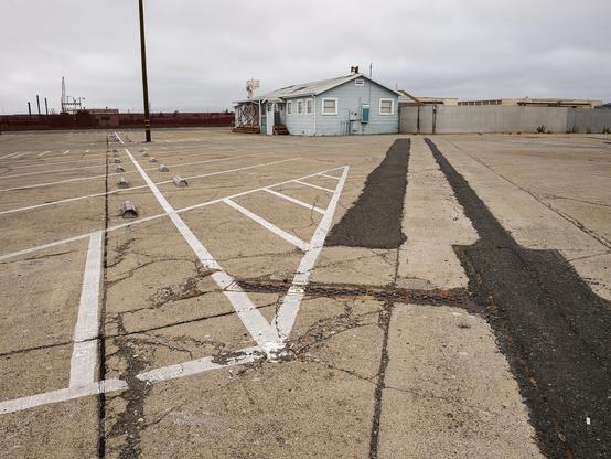 Concrete parking lot with guidelines and asphalt stripes leading in different directions, with naval building in background.