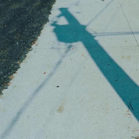 Blue shadow of a power pole with electrical transformed and powerlines on a wide sidewalk