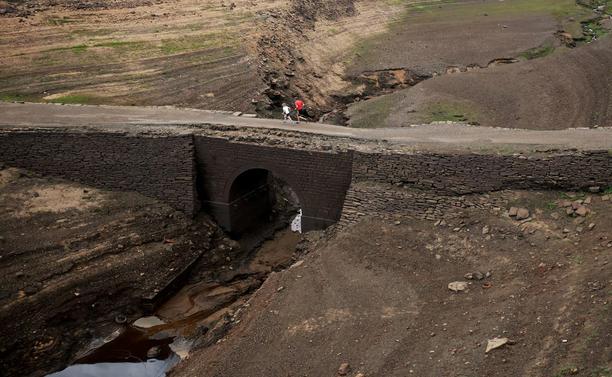 People run across an old Packhorse bridge in a dried out reservoir.