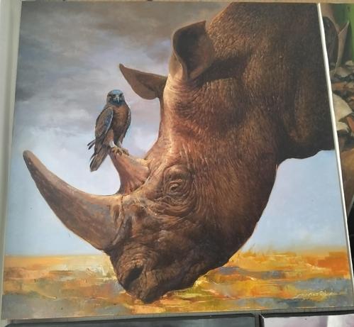 a painting of the side of a rhino, from his shoulders up, in a dry golden landscape, a blue and brown falcon-type of bird landed on his shorter horn, perched and looking alert and proud 
