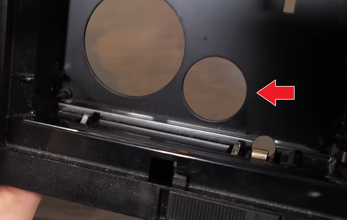 Screenshot of the video made by @TechConnectify@mas.to showing the VHS-C adapter with a red arrow, pointing on a second smaller hole right next to the big hole for the supply cog of the VHS-C tape. Screenshot of the video made by @TechConnectify@mas.to showing the VHS-C adapter with a red arrow, pointing on a second smaller hole right next to the big hole for the supply cog of the VHS-C tape.