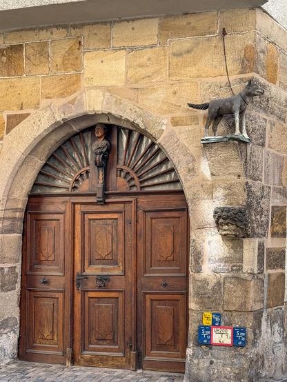 Wachhundskulptur an Hausecke oberhalb der geschnitzten 3 Holztüren in Torbogen