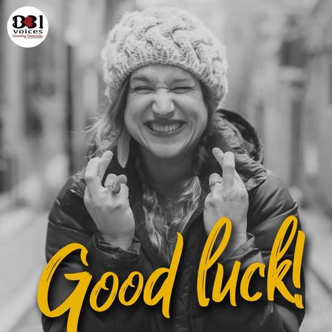 Woman smiling excitedly, eyes squeezed shut and fingers crossed. With the words ‘good luck’