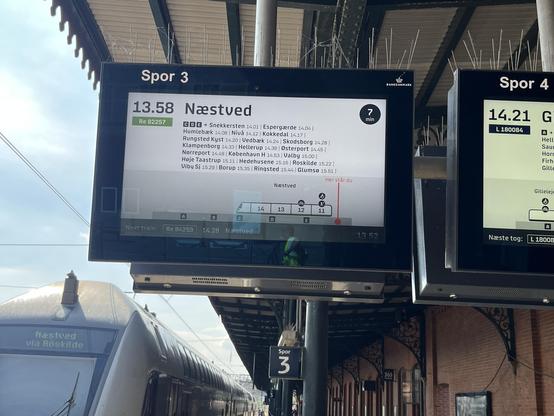 Infomonitor auf einem dänischen Bahnsteig, der alle Halte mit Uhrzeit, einen Wagenstand und "hier stehst du" auf einem Bild zeigt.