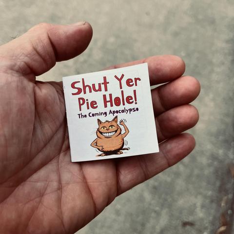 a human hand holds a tiny magazine called Shut Yer Pie Hole!