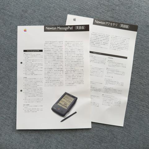 A pair of Japanese language documents are staggered on top of each other. The text contains descriptions, specifications, and other information pertaining to Apple’s original Newton MessagePad PDA and various accessories available for the system. Both documents are printed primarily in black and white. The topmost document has a rainbow Apple logo in the top left corner and a colour photo of the MessagePad device on the bottom right of the page.