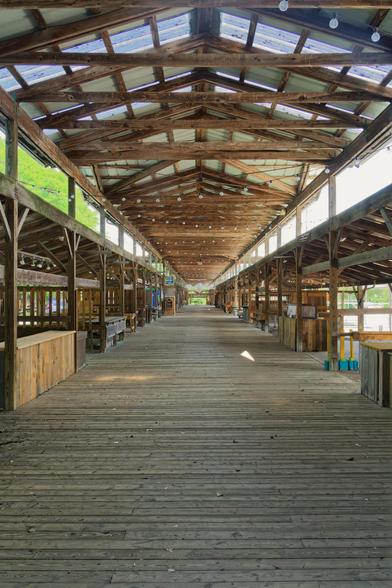 An empty wood-framed structure with a floor made ofthin wood boards;  there are the gaps between the main roof that covers the pedestrian area and the roofs covered vendor stalls that can be seen to the left and the right