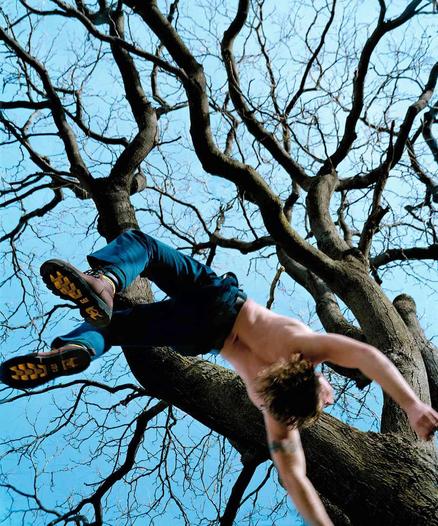 Man in jeans and boots falling from a tree against a clear blue sky.