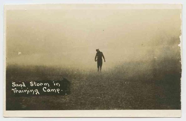 A lone figure walks through a hazy training camp during a sandstorm.