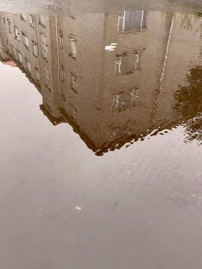 A building is reflected in a giant rain water puddle
