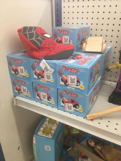 A stack of “flip over buggy” toys, probably dating from about the 80s, just hanging out NIB on a goodwill shelf. There are 13 of them, forming a cube of sorts, with one sticking out of the top of the stack. They are surrounded by miscellaneous items, including a Spider-Man hat.