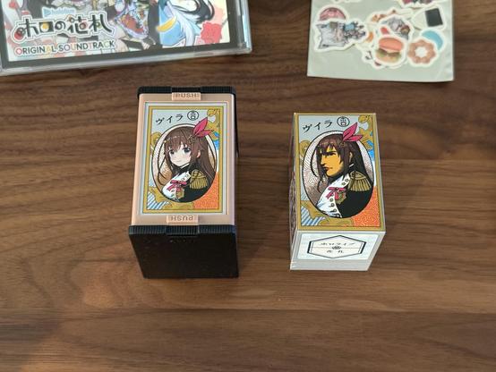 The box for the hanafuda deck, with the wrapped deck beside it. The wrapper shows the Napoleon art, but with Tokino Sora’s bow and hair accessory. The box features a Napoleon with Sora’s face instead. 