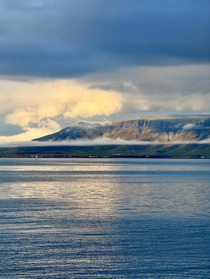 My Esja over the water. The left slope has bright white clouds, while the near flank is bathed in sunlight. There’s a layer of fog along the bottom third of the mountain. Stunning. 