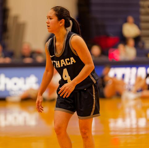 A woman with hard hair tied back wearing blue shorts and a tank top that says ITHACA 4