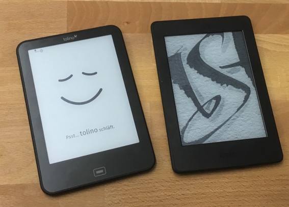 Ein Tolino und ein Kindle nebeneinander auf einer Holzfläche liegend