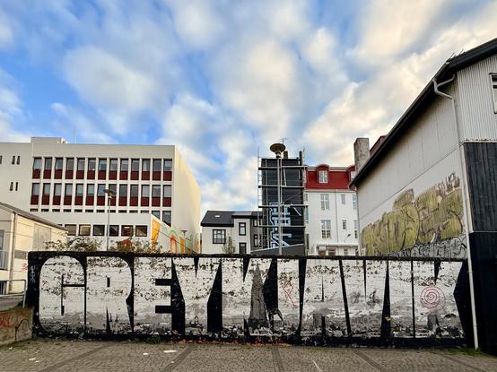 A mural that spells out “greykjavík” in all caps with the skyline of Reykjavík in the letters. The sky above is filled with puffy white clouds