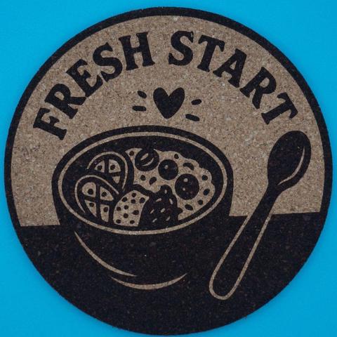 Korkuntersetzer lasegraviert mit der Aufschrift Fresh Start und einer Müslischüssel mit einem kleinen Herz drüber und einem Löffel daneben.