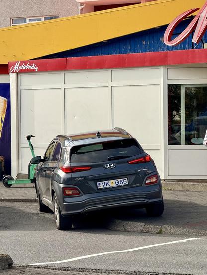 A car is half straddling the sidewalk and half in a perfectly good parking space in front of Melabúðin 