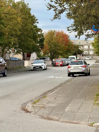 A car is parked on the sidewalk while there are at least two or three legal parking spaces across the road