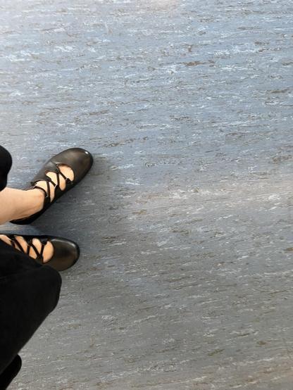 Füße in schwarzen, offenen Schuhen auf blau-grauem Linoleum