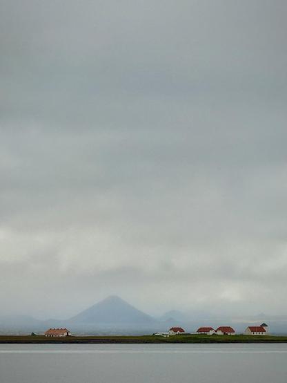 Keilir mountain is seen shrouded in fog across the water. There are some red-roofed buildings along the shore