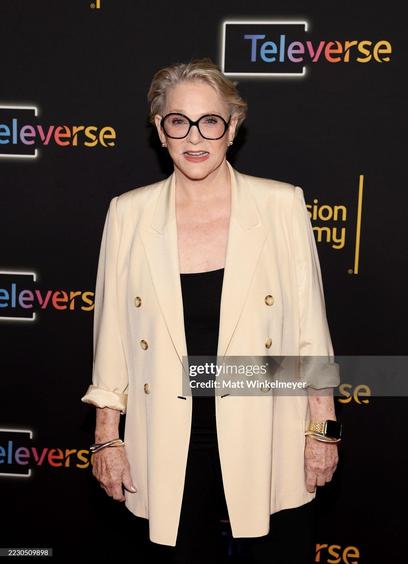 Sharon Gless on the red carpet. She wears black pants, a black shirt, a champagne-colored jacket and black-framed glasses.