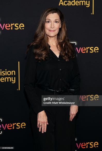 Thea Gill on the red carpet. She wears an all black jumpsuit with a leather belt. Her long hair is brown nowadays.