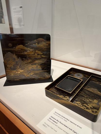a lacquered inkstone box from the 1600’s with mountain views in gold. the lid of the box is particularly ornate. the inner part of the box is divided into sections for the inkstone and water (?)