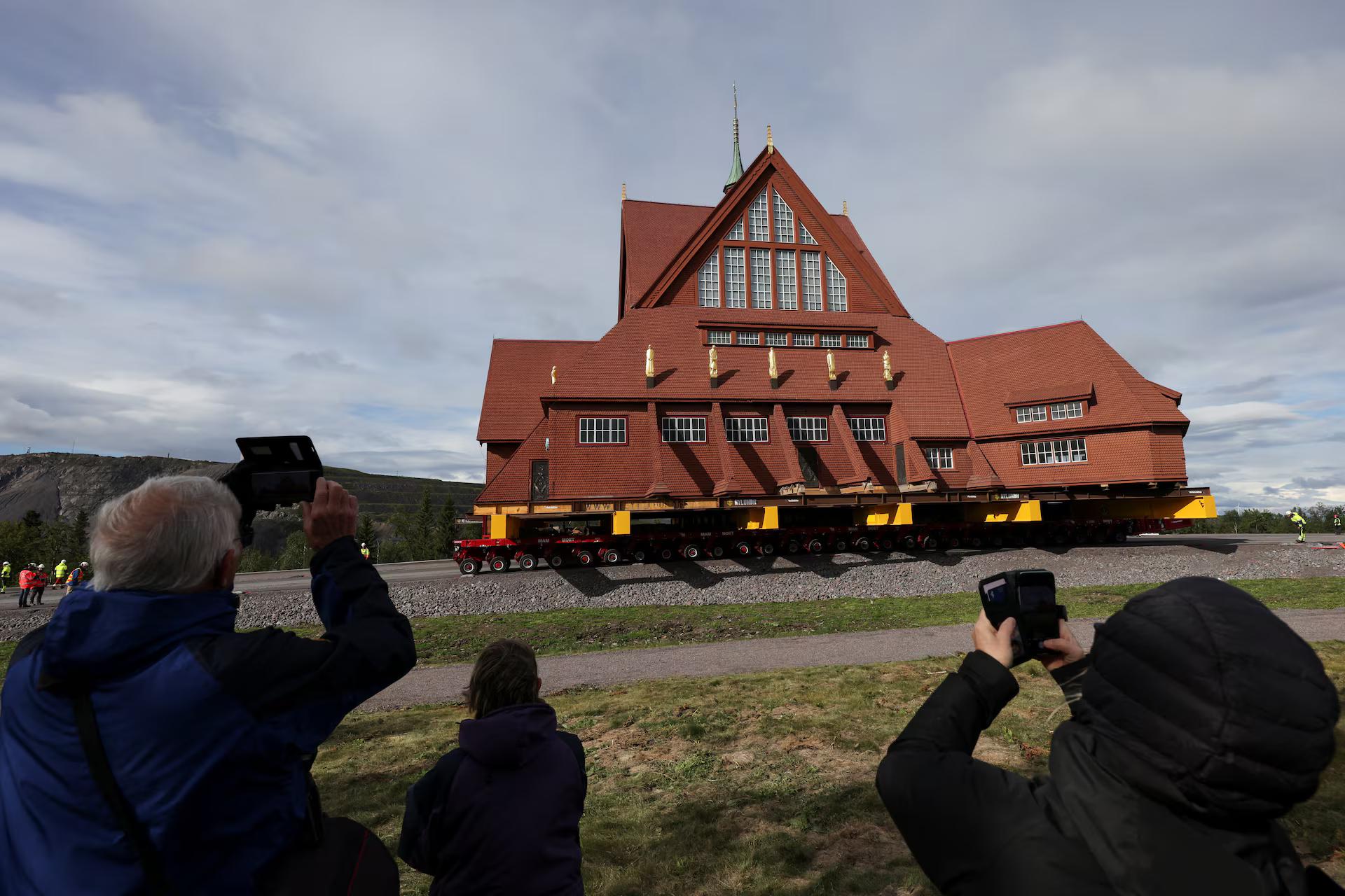 People use their mobile phones as Kiruna's old wooden church is moved during a two-day relocation trip to a new site next to a cemetery. People use their mobile phones as Kiruna's old wooden church is moved during a two-day relocation trip to a new site next to a cemetery.