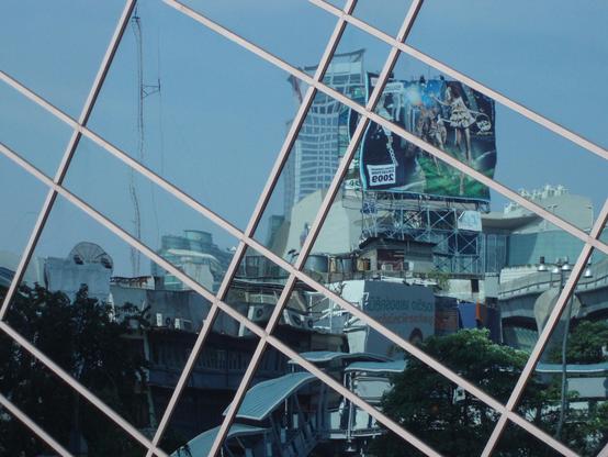 In einem Spiegelglassfenster mit verschiedenen Unterteilungen brechen sich die Gebäude und die Werbetafeln und sehen dadurch ganz anders aus in ihrer neuen Zusammensetzung