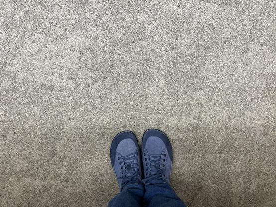 Füße in blauen Sneakern auf beigem Teppich