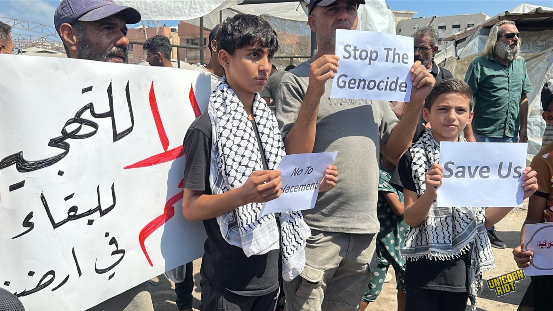 Hundreds of Palestinians in Gaza City march against Israeli's war on Gaza and forced displacement. Youth hold signs in English saying "No To Displacement" and "Save Us." Adult men hold signs, one in Arabic, and another in English reading "Stop The Genocide" - August 21, 2025