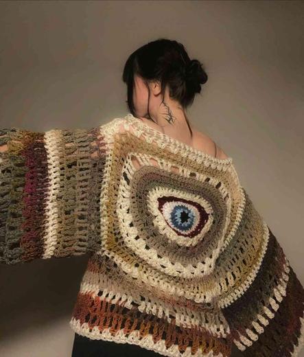 Woman with dark hair in a bun wearing a multicolored crocheted top with an eye pattern.