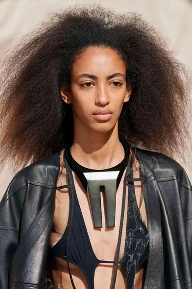 Model with voluminous natural hair wears a black leather jacket and a striking silver pendant necklace.