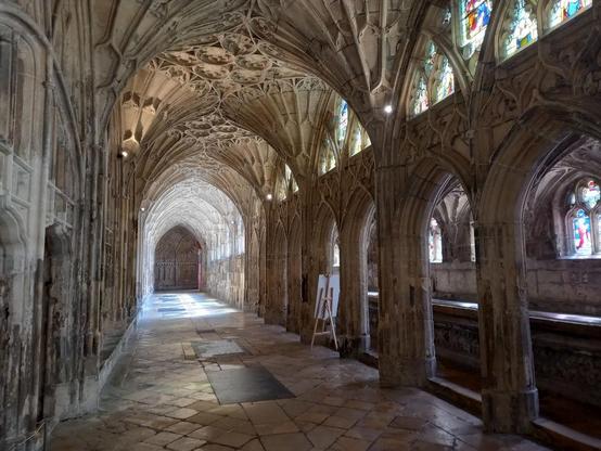 A view down a cloister. Walls of white stone. Ceiling of white stone and with intricate fan vaulting.